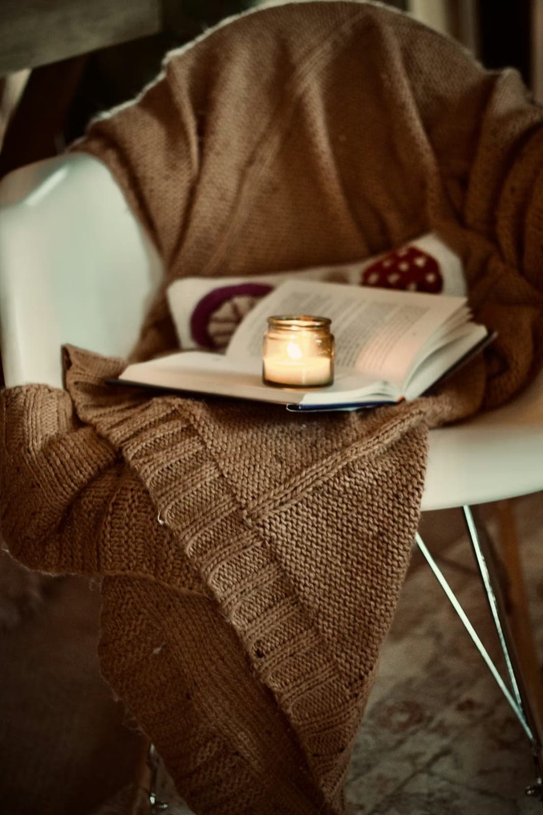 A quiet armchair with an open book and a lit candle — a calm space for reflection.