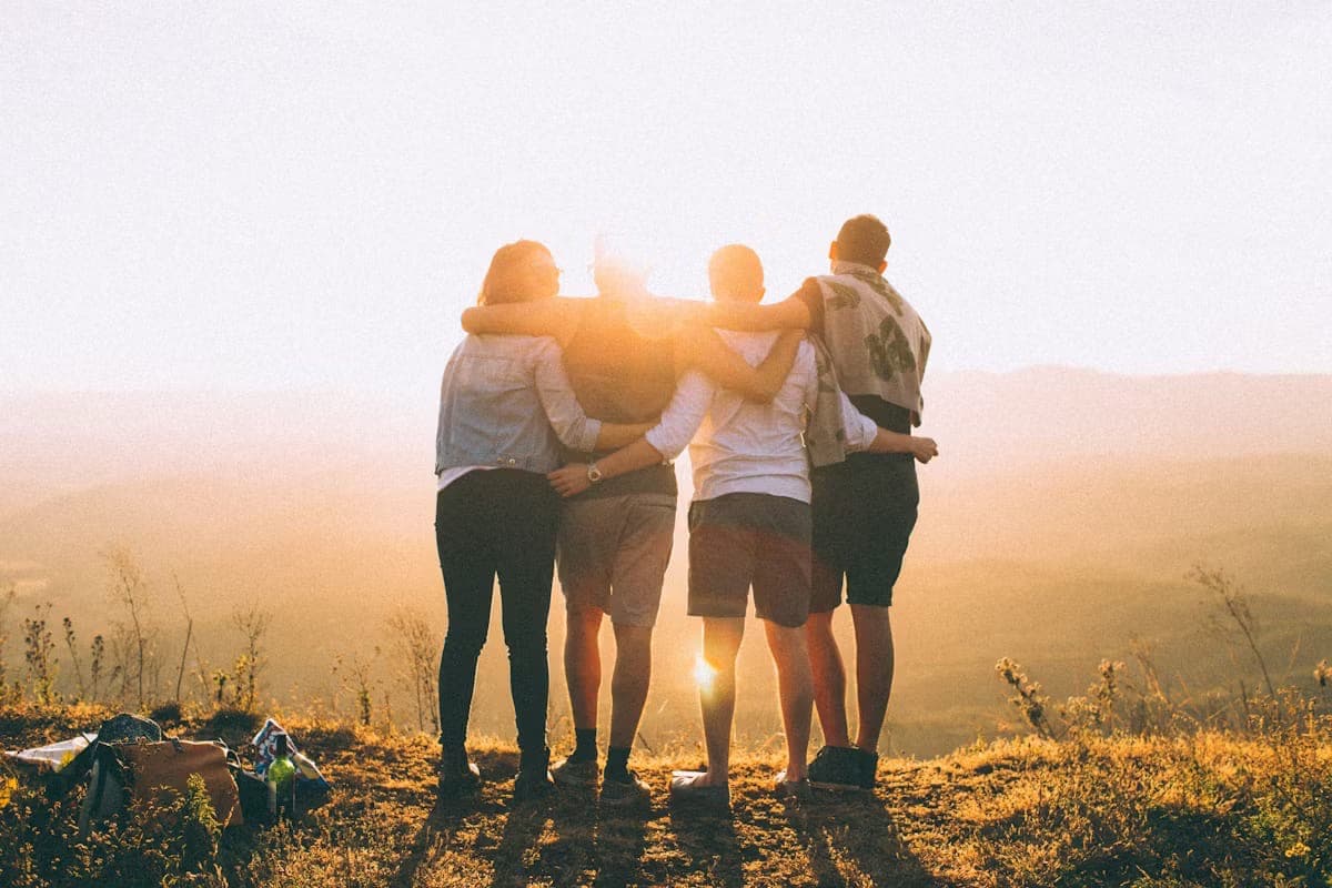 Four friends arm-in-arm at sunset looking out over rolling hills — connection and belonging.
